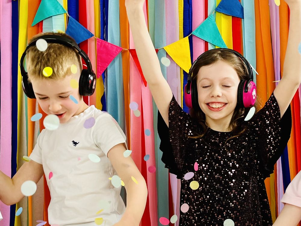 Two children wearing Hushify wireless silent disco headphones, dancing together and celebrating